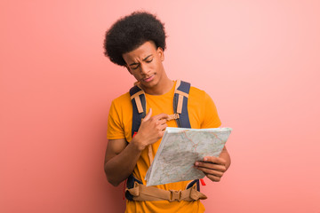 Young african american explorer man holding a map smiling confident and crossing arms, looking up