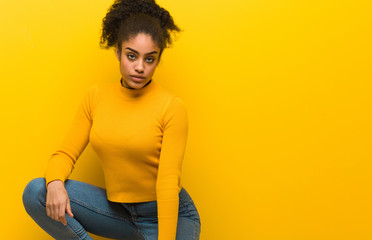 Young black woman sitting over an orange wall