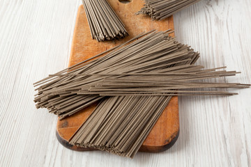 Fototapeta na wymiar Uncooked buckwheat soba noodles on rustic wooden board over white wooden background, side view.