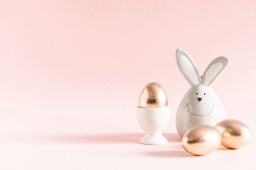 Naklejka na ściany i meble Easter golden eggs and porcelain rabbit on pastel pink background. Easter, spring concept. Copy space, banner
