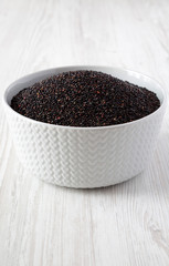 Gluten free raw organic black quinoa in a bowl over white wooden surface, side view. Close-up.