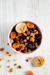 Top view, dried fruits and nuts in a pink bowl over white wooden background. Overhead, from above, flat lay. Space for text.