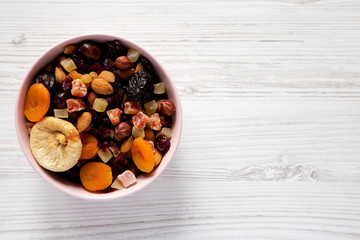 Dried fruits and nuts in a pink bowl over white wooden background. Top view, from above, flat lay. Space for text.