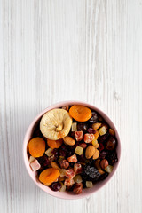 Dried fruits and nuts in a pink bowl over white wooden surface. Top view, from above, flat lay. Copy space.