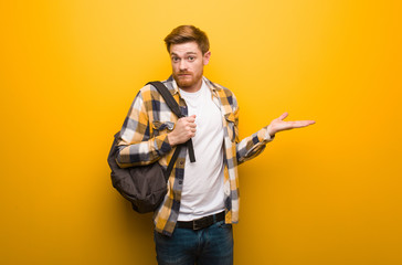 Young redhead student man doubting and shrugging shoulders