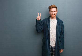 Young redhead man in pajama fun and happy doing a gesture of victory