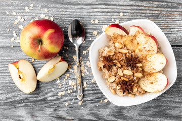 Oatmeal with apple and cinnamon on gray wooden background.