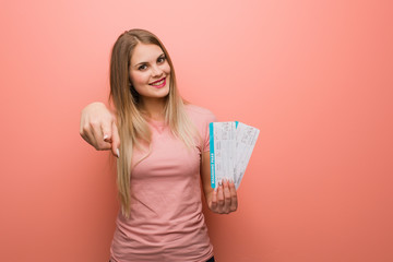 Young pretty russian girl cheerful and smiling pointing to front. She is holding an air tickets.
