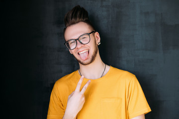 Portrait of funny guy with trendy comb over haircut. Handsome emotional man sticking tongue out,...
