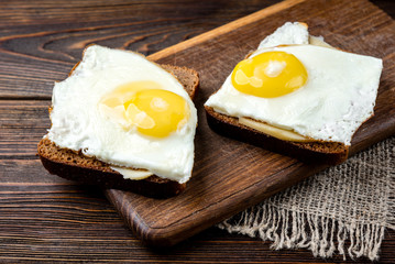 Bread with cheese and eggs on dark wooden background.