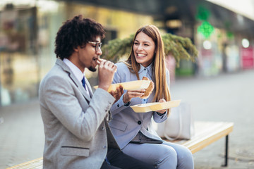 Smiling businessmen with sandwiches sitting in front of the office building - lunch break
