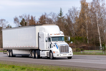 Long haul white big rig semi truck transporting goods in dry van semi trailer running on straight...