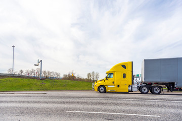 Profile of bonnet big rig yellow semi truck with dry van semi trailer driving on wide highway to warehouse