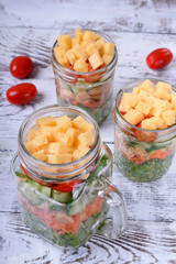 Layered salad with cheese, kale, carrot, chicken, cucumbers and cherry tomatoes in glass mason jars