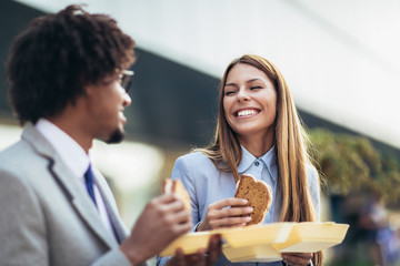 Smiling businessmen with sandwiches sitting in front of the office building - lunch break
