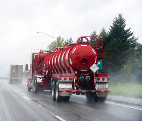 Red big rig semi Truck with tank semi trailer for transportation of chemicals and toxic liquids running on the raining road