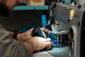 A master sews parts on a sewing machine for a future product made of genuine leather