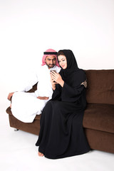 Arab muslim married couple using smart phone while sitting on sofa chair at home