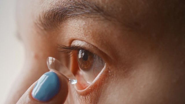 A beautiful young girl puts contact lenses in her eye close-up, macro. Blinking distributes the lens in the pupil. Brown eyes, black eyelashes, transparent lenses. Slow motion, 4K
