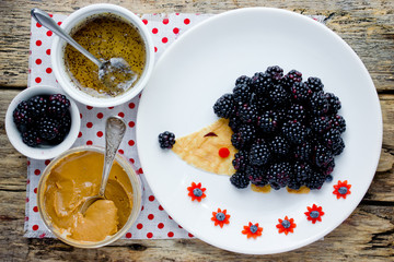 Fun and healthy breakfast for kids - edible hedgehog from pancake with peanut butter and fresh blackberry,  animal shaped food art idea
