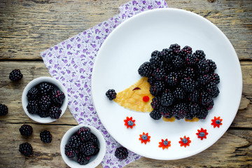 Fun and healthy breakfast for kids - edible hedgehog from pancake with peanut butter and fresh blackberry,  animal shaped food art idea