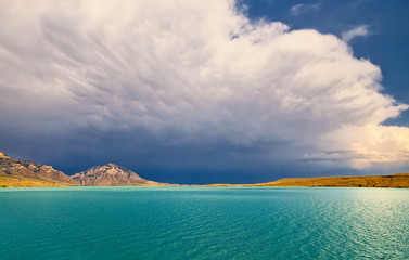 Beautiful aqua water with mountains and a valley in the distance under a cloudy blue sky in a summer Wyoming landscape