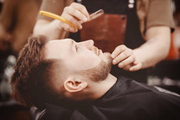 Obraz na płótnie Canvas Man Barber shaves beard of client on chair Barbershop