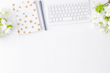 Flat lay blogger or freelancer workspace with a notebook, keyboard and white spring flowers on a white table