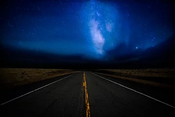  Een snelweg die in de verte verdwijnt, verlicht door een met sterren gevulde dramatische nachthemel in een landelijk landschap © kat7213