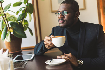 Young handsome dark-skinned businessman drinks coffee in a cafe.