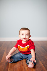 Naklejka premium Happy Baby Boy Sitting on Wood Floor in Home - Color Portrait