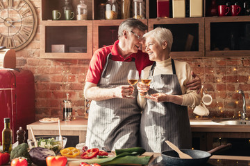 Cheerful senior couple clinking with wine glasses in kitchen