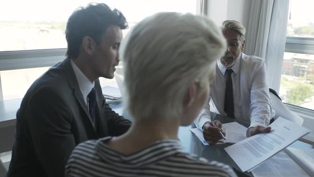Medium shot of businessman explaining document to his colleagues while using digital tablet in office