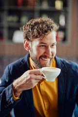 Portrait of young modern Caucasian man dressed smart casual sitting in cafeteria and drinking fresh coffee.