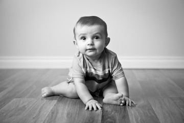 Naklejka premium Happy Baby Boy Sitting on Wood Floor in Home - Black and White