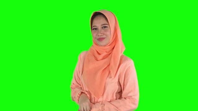 Cute young female muslim model smiling and posing at the camera in the studio while wearing islamic clothes. Shot in 4k resolution with green screen background