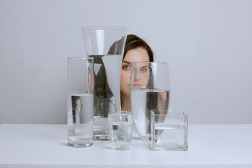 Art portrait of young beautiful woman. Distorted reflection in glass vases with water.