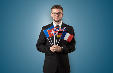 Cheerful student standing in front of wall with national flag on his hand
