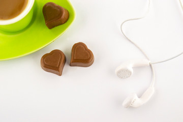 Coffee in a green cup with heart-shaped chocolate and headphones on a white background. Top view.
