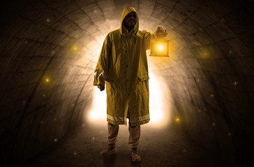 Ugly man in raincoat walking with glowing lantern in a dark tunnel