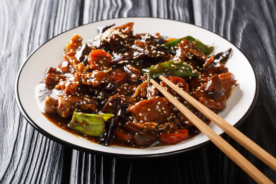 Asian main dish of roasted pork with mun mushrooms and vegetables in a spicy sauce closeup on a plate. horizontal