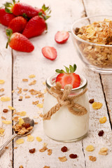 Jar with delicious yogurt and strawberry and granola muesli, over a white on wooden table