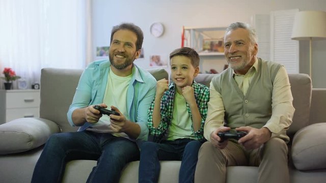Preteen boy cheering for dad and granddad playing video game, pappy time, hobby