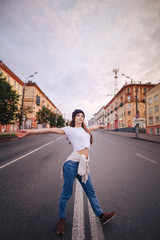 Girl posing in the middle of the roadway. Girl in stylish clothes and hat.