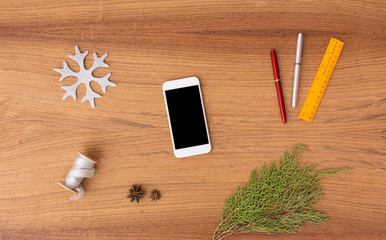 smart phone mobile display on table with isolated white screen for mockup in Christmas time. Christmas tree, gifts, decorations in background.