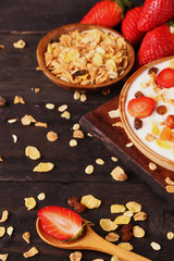 Bowl of yogurt with strawberries and granola muesli, over a white wood background.
