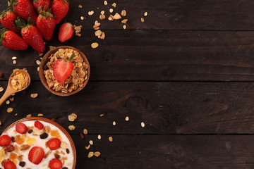 Bowl of yogurt with strawberries and granola muesli, over a white wood background.