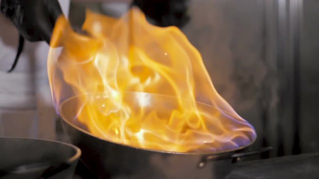 Chefs cooks and doing flambe on vegetables in wok on restaurant kitchen