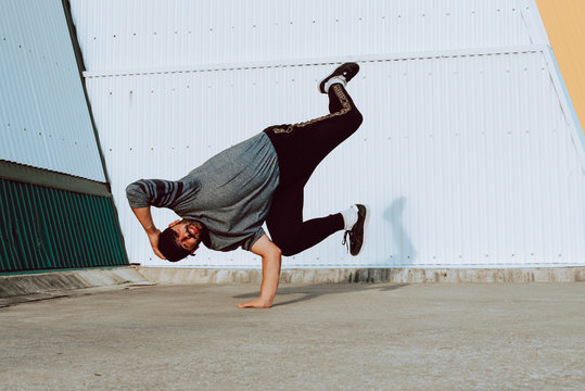 Attractive guy performing handstand and while dancing near wall of modern building on city street
