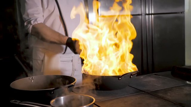 Chefs cooks and doing flambe on vegetables in wok on restaurant kitchen